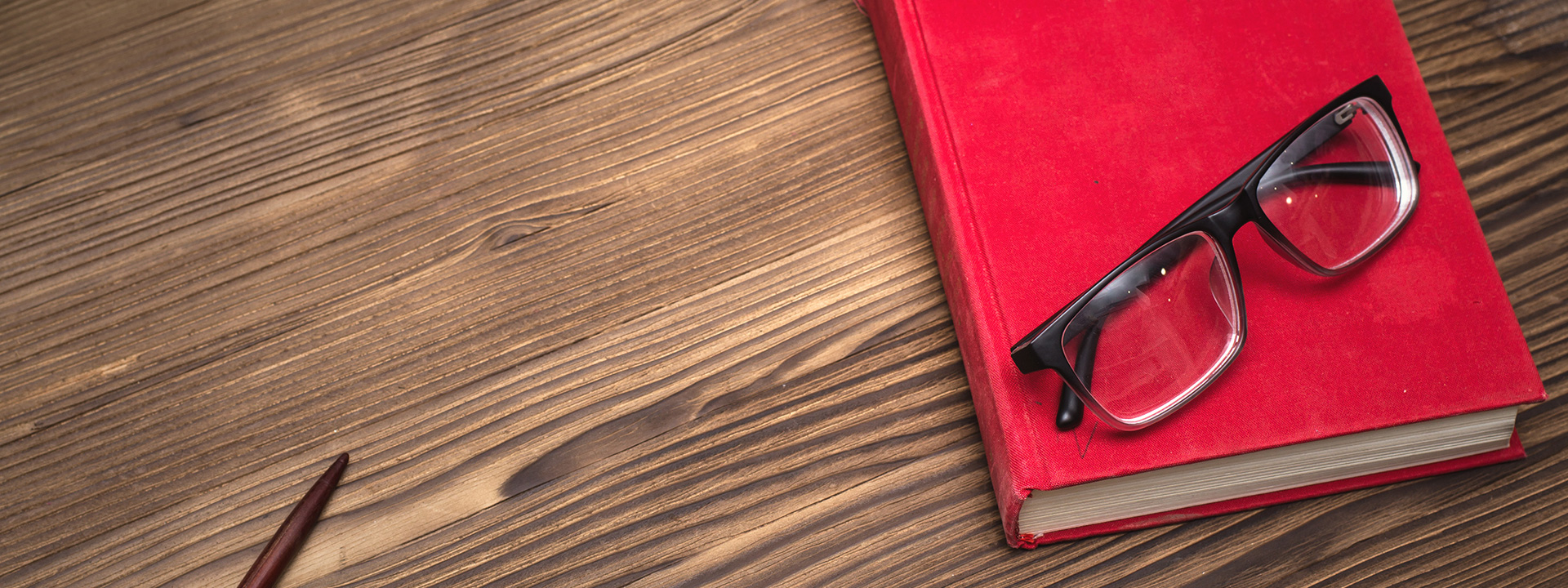 Red notebook sitting on a wood table. Reading glasses are sitting on the notebook.