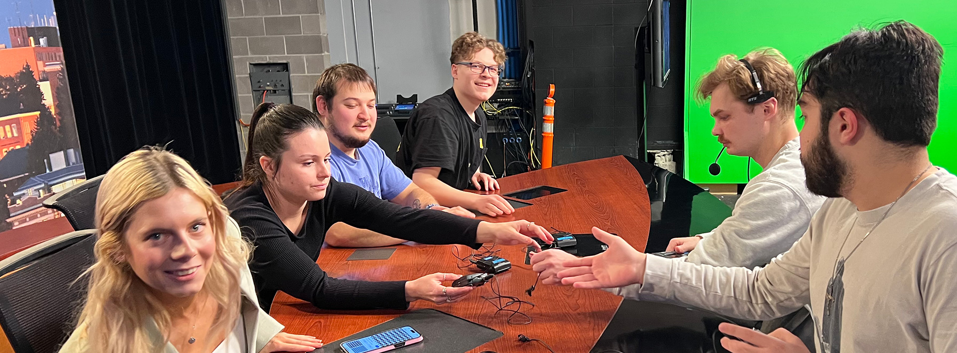 Group of students sitting at a table in a greenroom getting ready to broadcast the news.