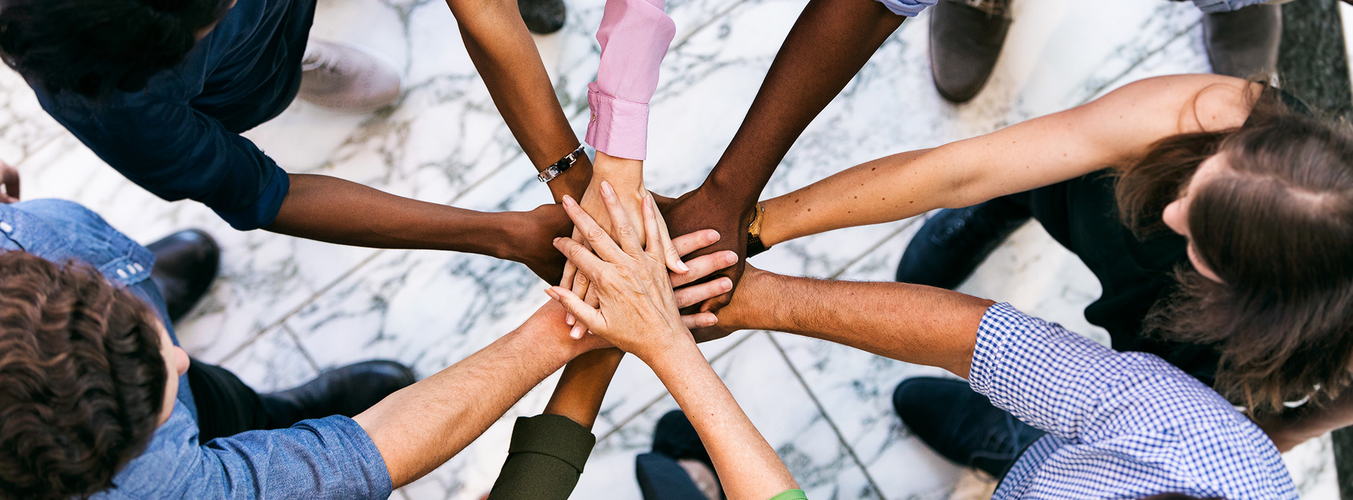 People of different ethnicity holding hands in a go team huddle