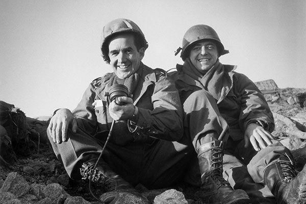 Edward R. Murrow sites next to a man on rocks in army uniform