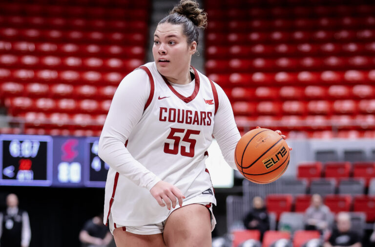 Woman looking up court dribbling basketball, wearing white uniform, crimson trim with "Cougars 55" written on the front.