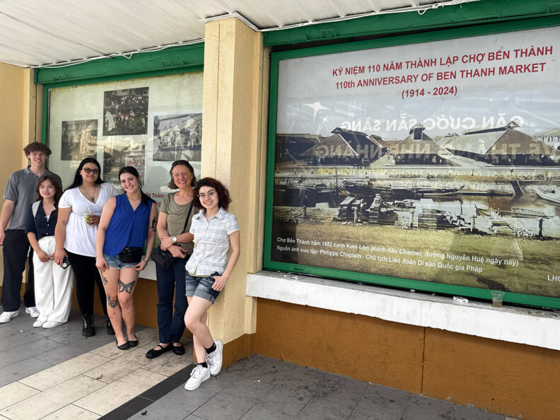 WSU Murrow College Backpack Journalism student Andrew Perdue, translator An Nguyen, students Olivia Soliz and Grace Harvey, Assistant Professor Alison Boggs and student Arlo Popa stand outside the Ben Thanh Market in Ho Chi Minh City, Vietnam