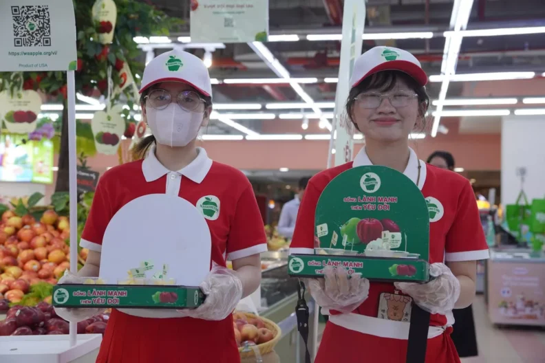 Two WinMart grocery store employees presenting apple samples to customers. Wearing white baseball caps, red uniforms.