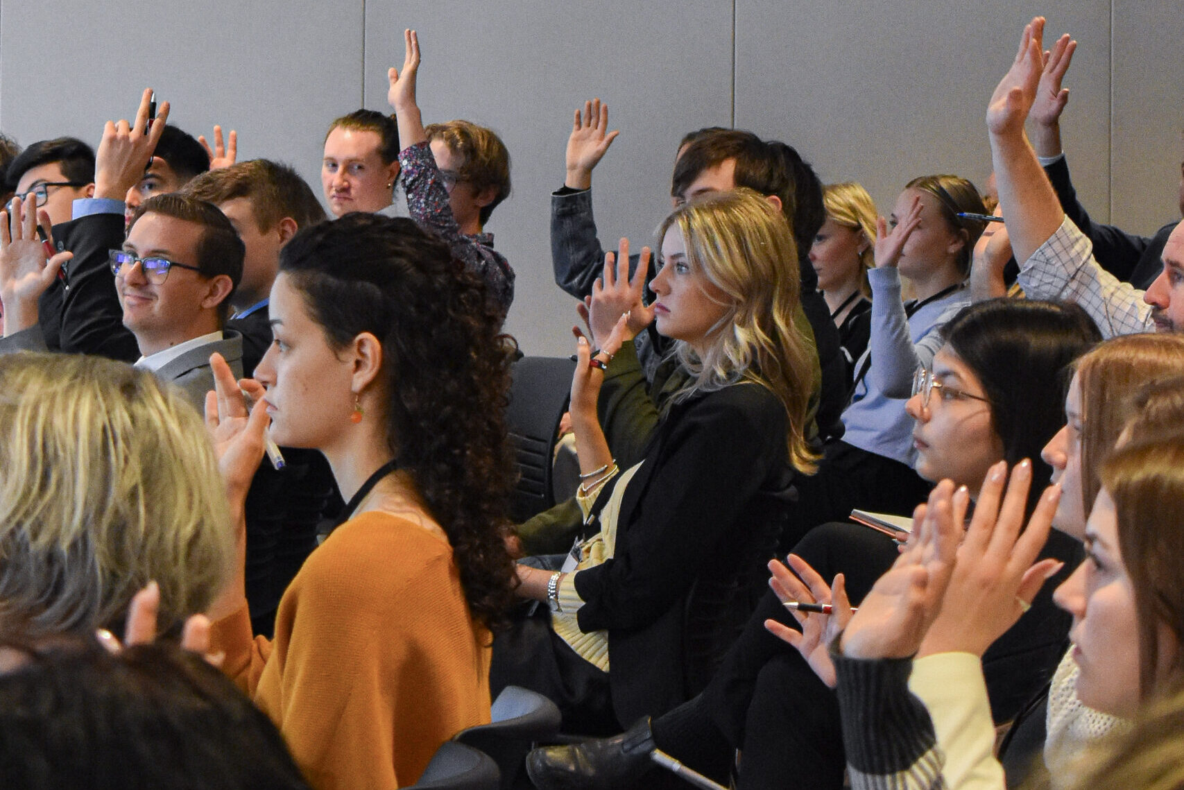 An audience of people is standing and raising their hands