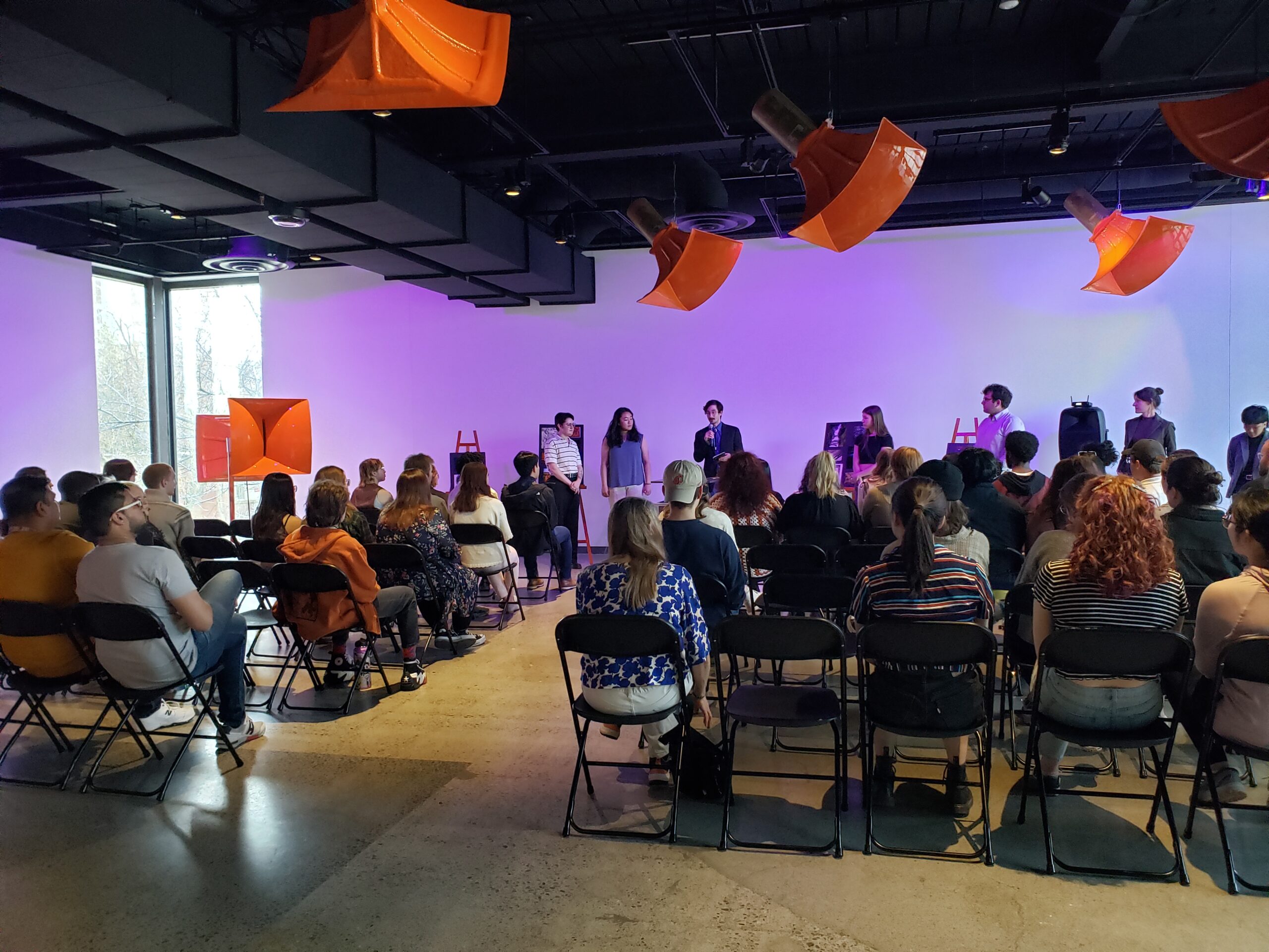 A crowd of seated people in a room with purple light.