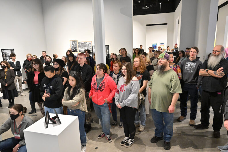 A crowd of people in the museum art gallery listening to a talk.