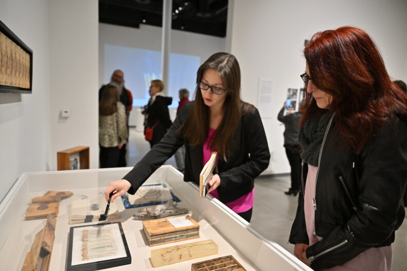 Shanda Stinebaugh pointing at her artwork in a display case in the museum gallery