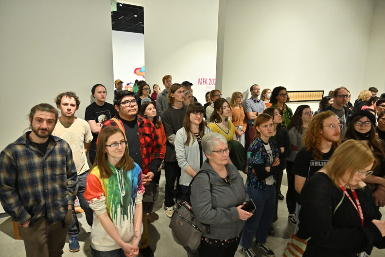 A crowd of people in the museum gallery listening to a talk.