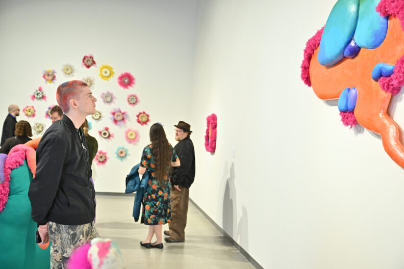People in the art gallery viewing colorful ceramic and multimedia artwork.