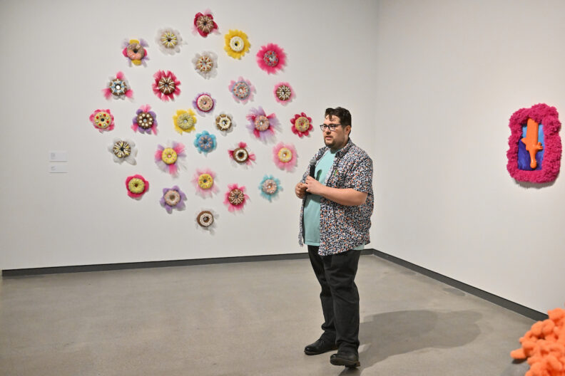 Adam Stuart speaking into a microphone in front of his artworks.