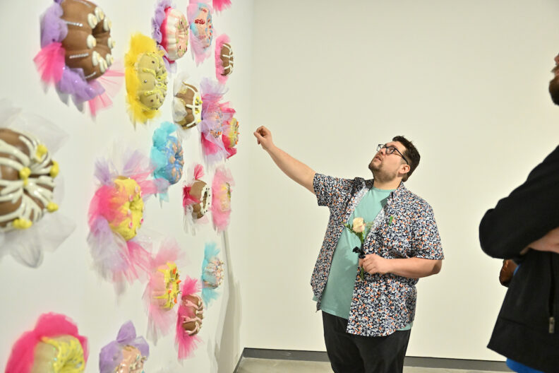 Adam Stuart gesturing towards his ceramic artwork on the museum gallery wall.