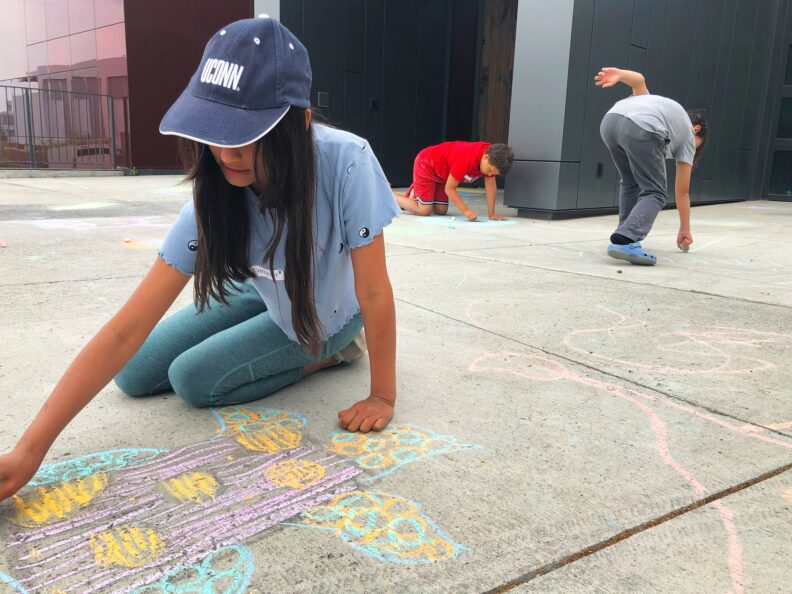 Three fifth grade students creating chalk drawings on the ground in front of the art museum.