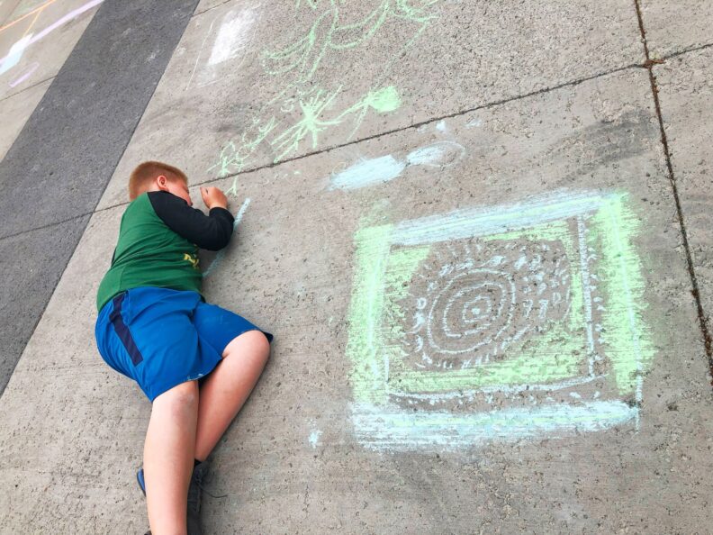 A fifth grade student creating green and blue chalk drawings on the ground in front of the art museum.
