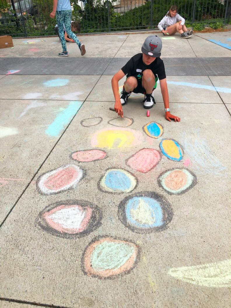 A fifth grade student creating a chalk drawing on the ground in front of the art museum.