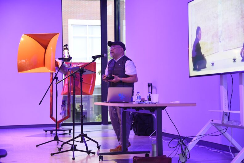 Sam Roxas-Chua speaks into a microphone next to a presentation.