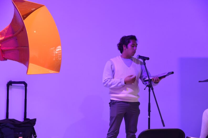 A speaker reads from a book into a microphone.