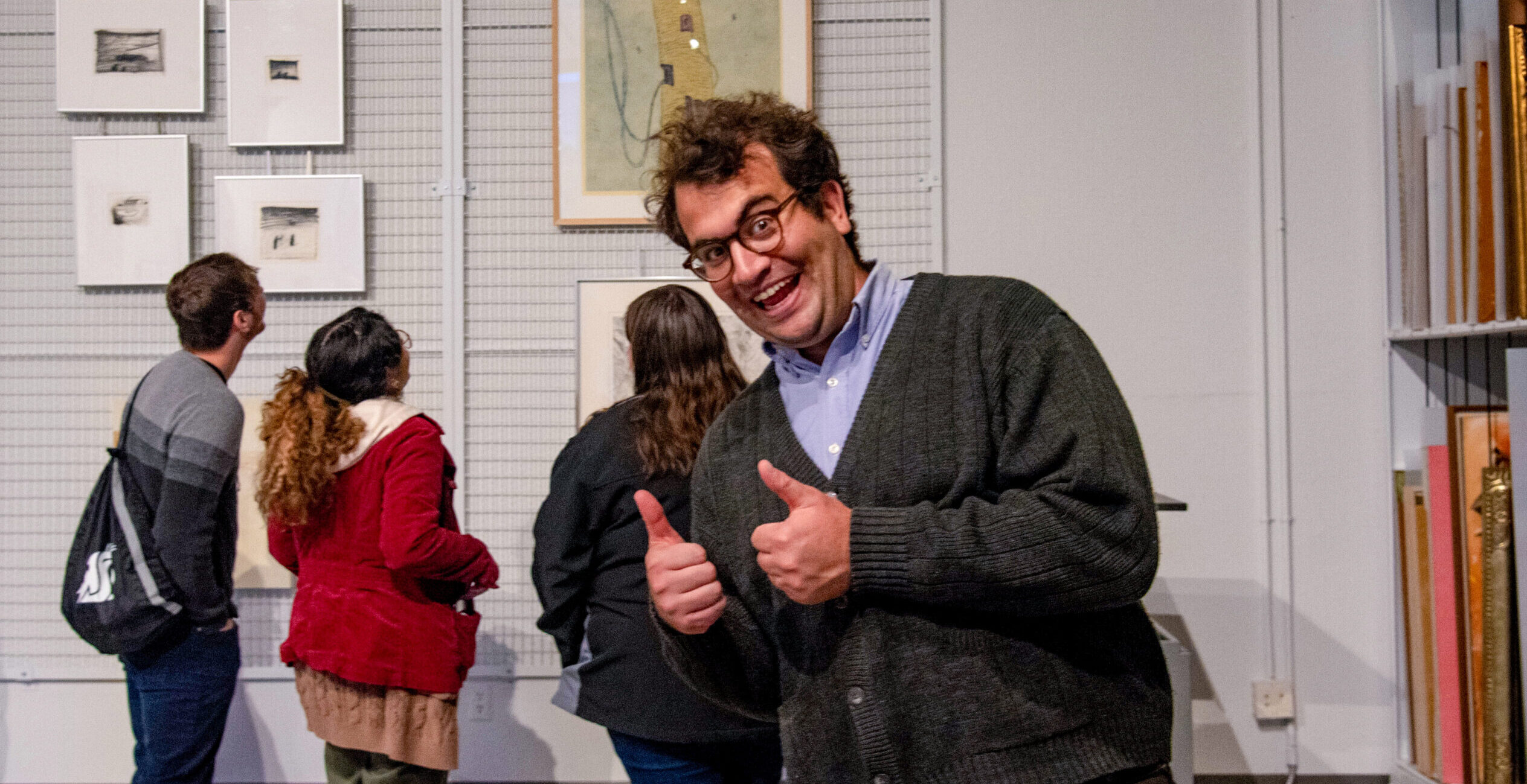 Man giving thumbs up sign in front of art lovers looking at paintings