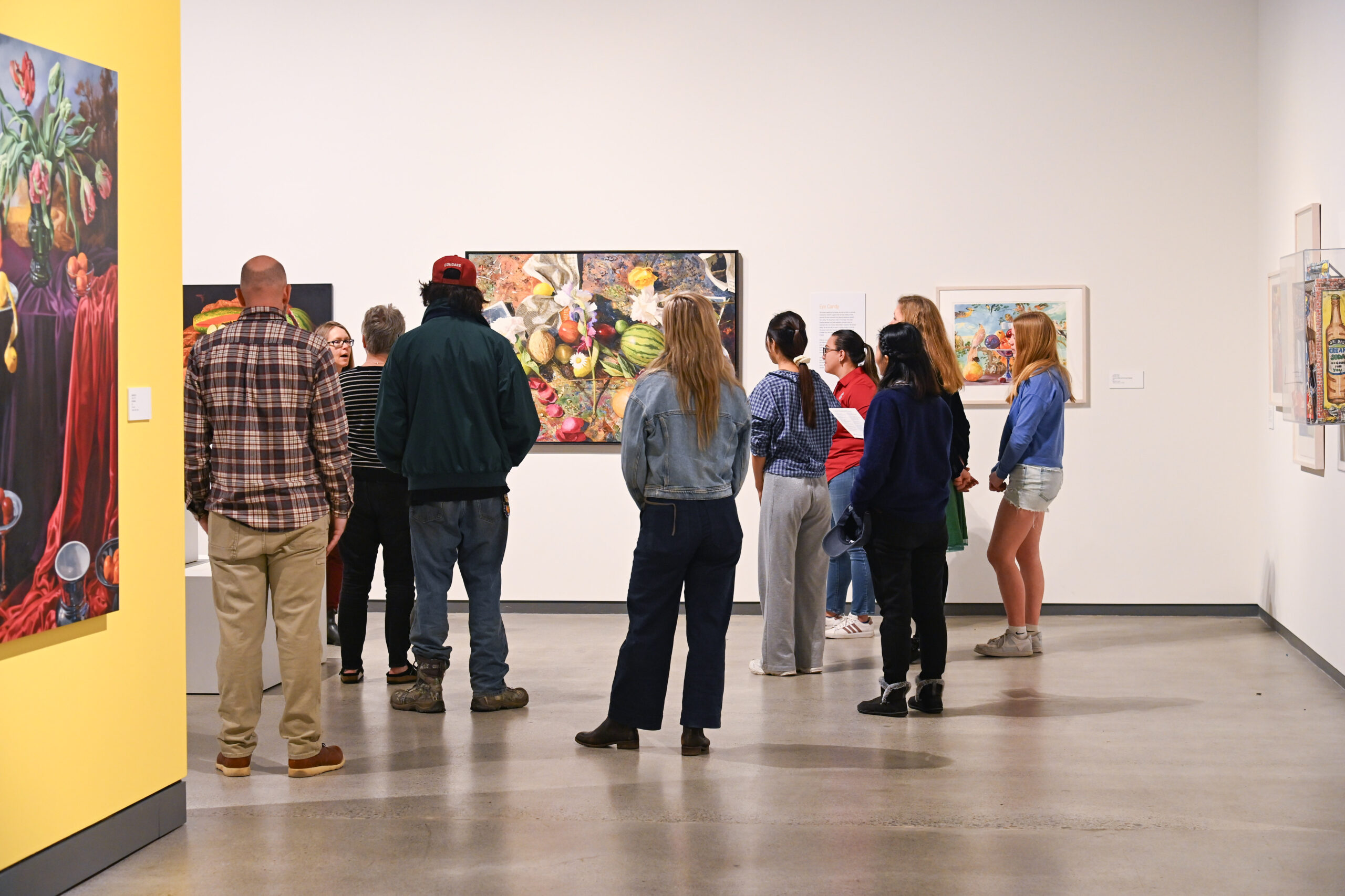 A tour group listens to a museum curator in front of colorful art depicting food.
