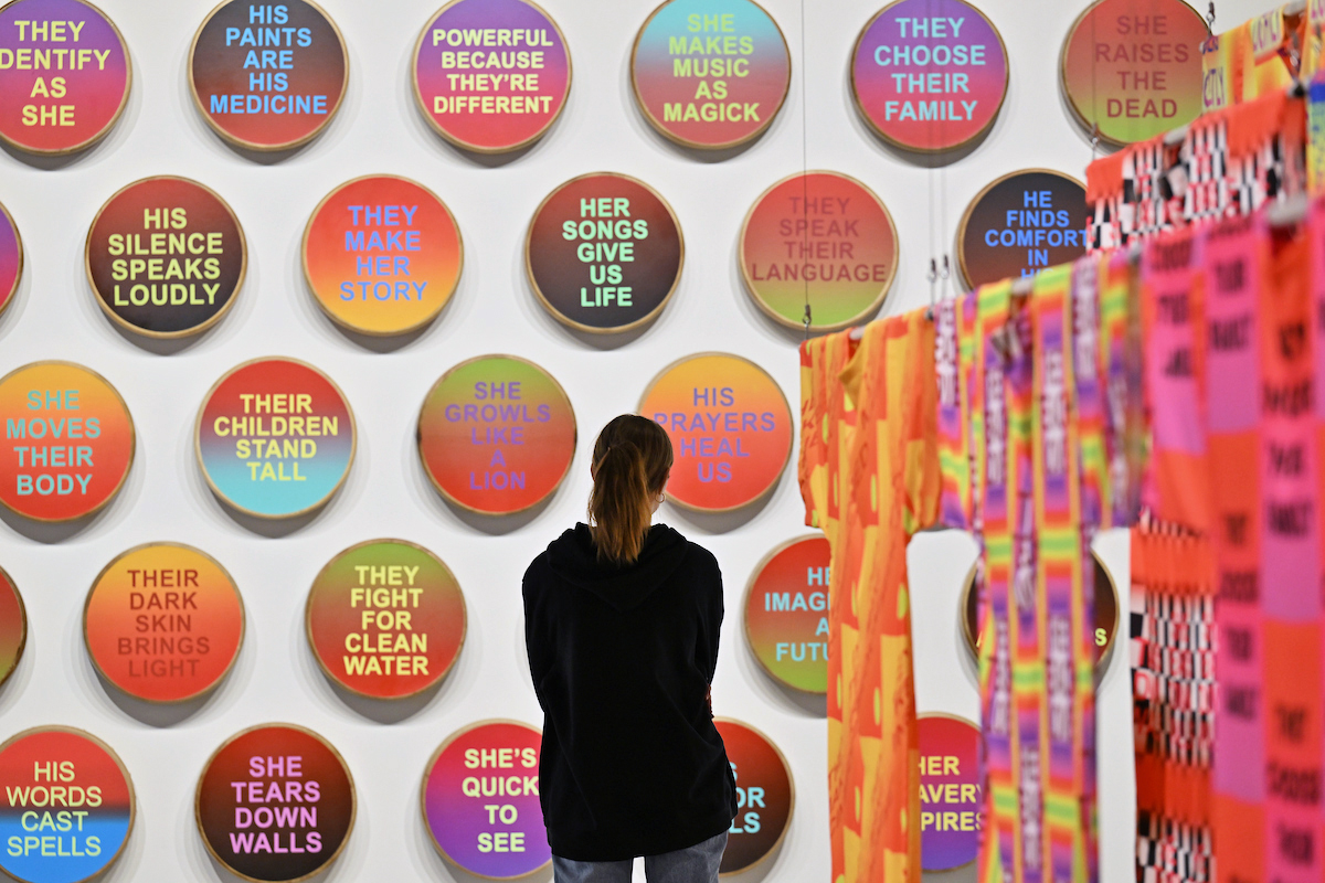 A visitor observes a colorful set of elk hide drums hung on the gallery wall.