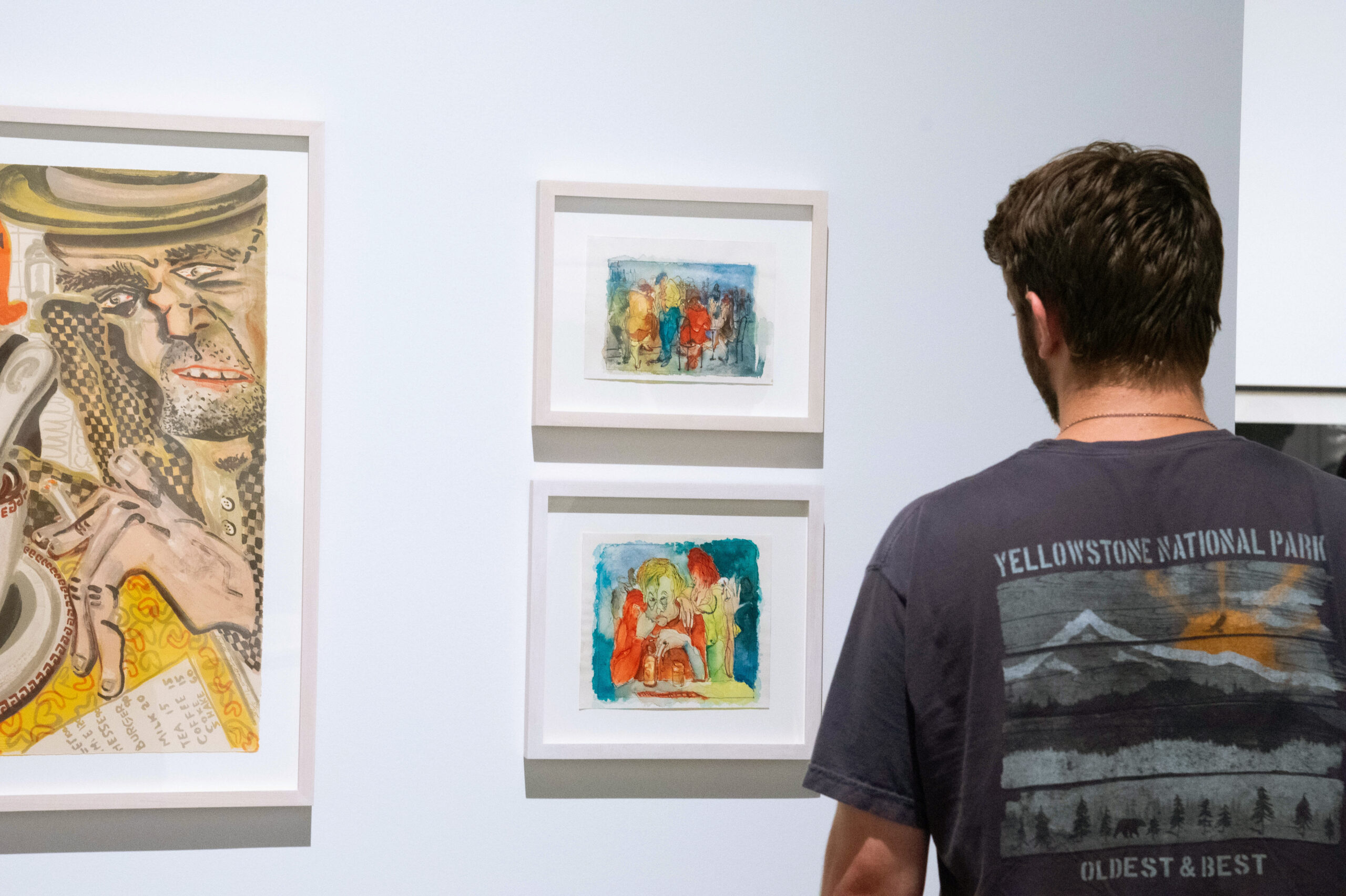 A student observes two watercolor paintings hanging on a wall.