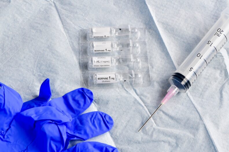 Close-up of liquid morphine sulphate glass vial for injections or infusion, blue glove and empty syringe