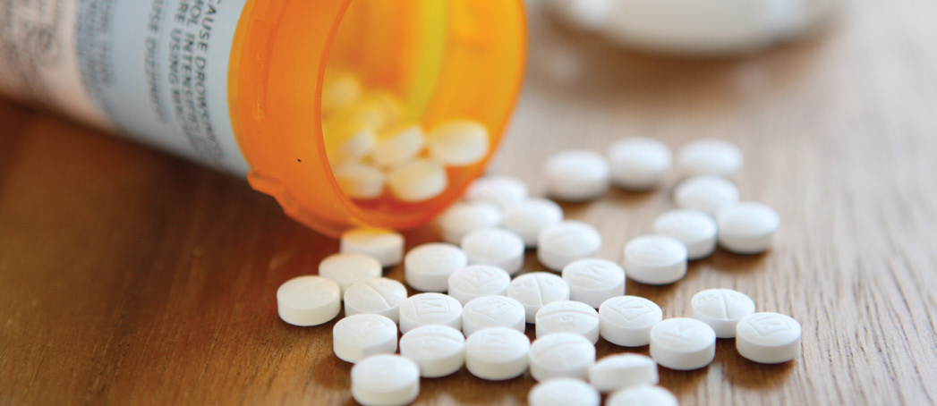 Open bottle of prescription pills scattered on a table top surface.