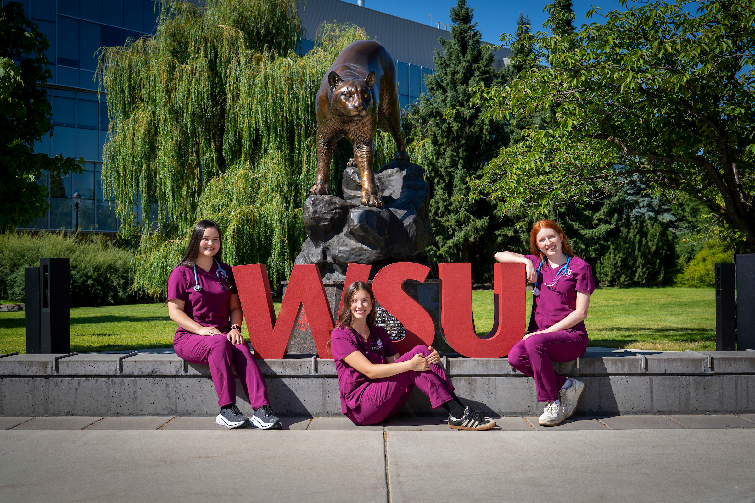 Three female nursing students sitting in front of the WSU Spokane cougar statue.