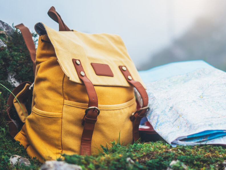 Photo of a yellow backpack and a map in the outdoors. 