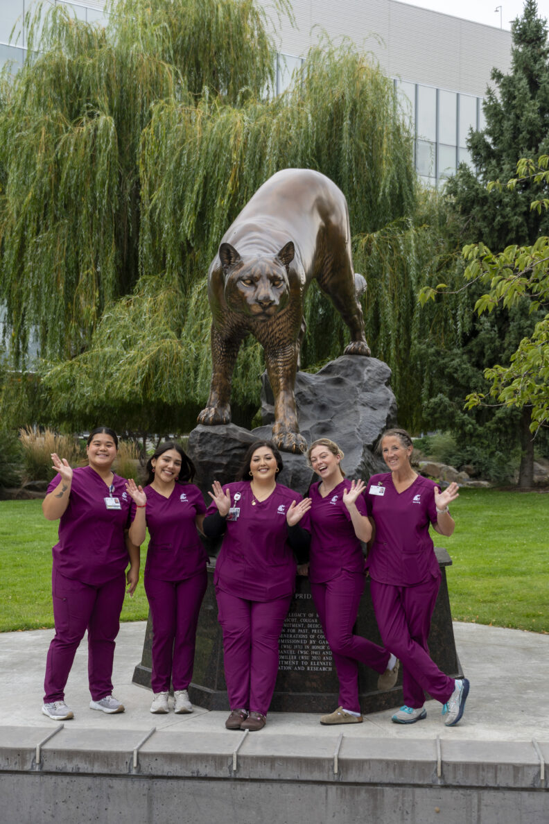 Nursing students waving in front of the WSU Cougar statue on the Spokane campus.