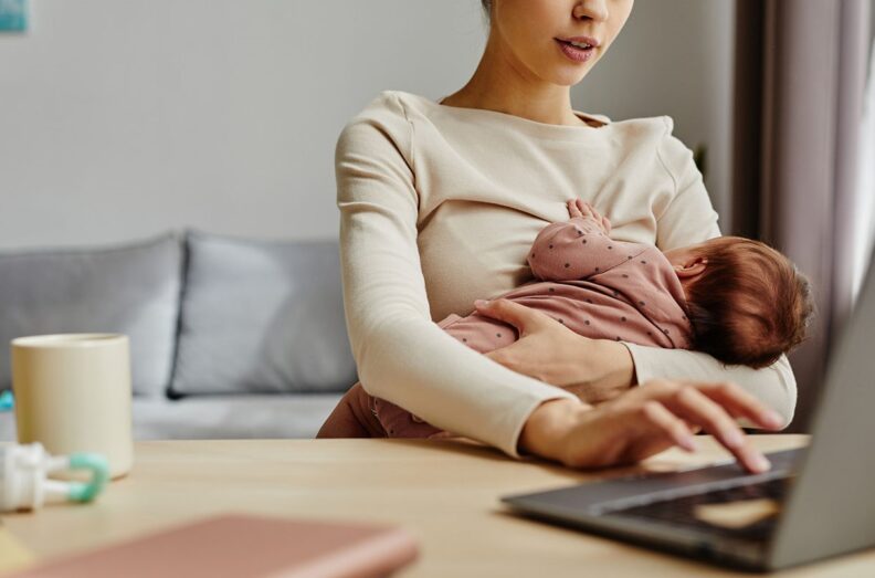 3D rendered illustration of a mother breastfeeding a child while working on a laptop at a table in a home environment.