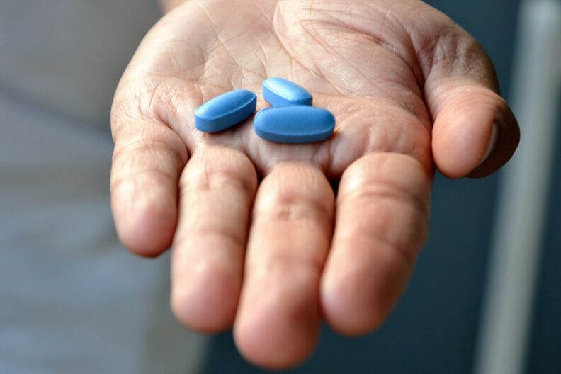 An open hand holding three blue pills.