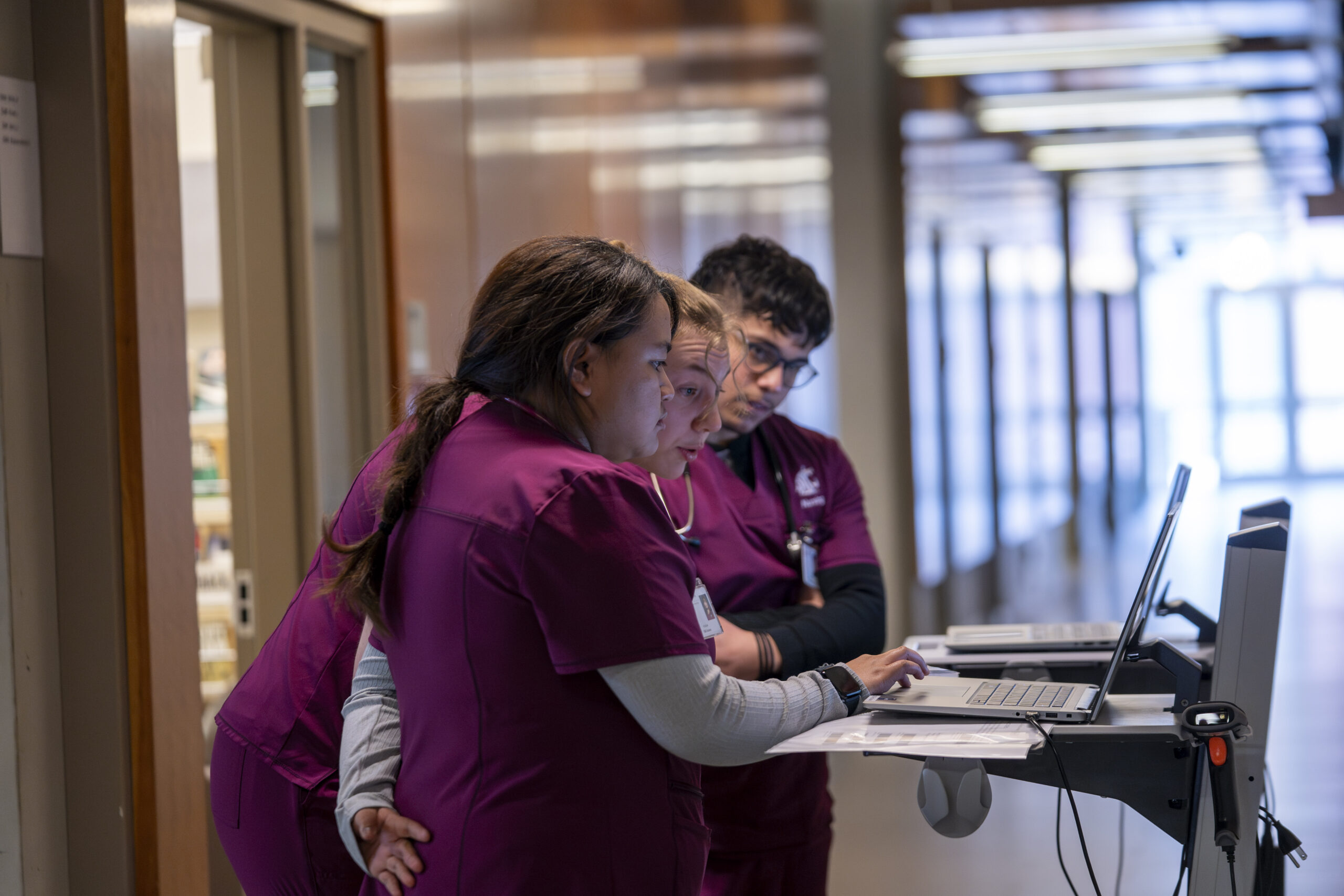 Three nursing students huddled around a laptop as they prepare to enter a simulation scenario.