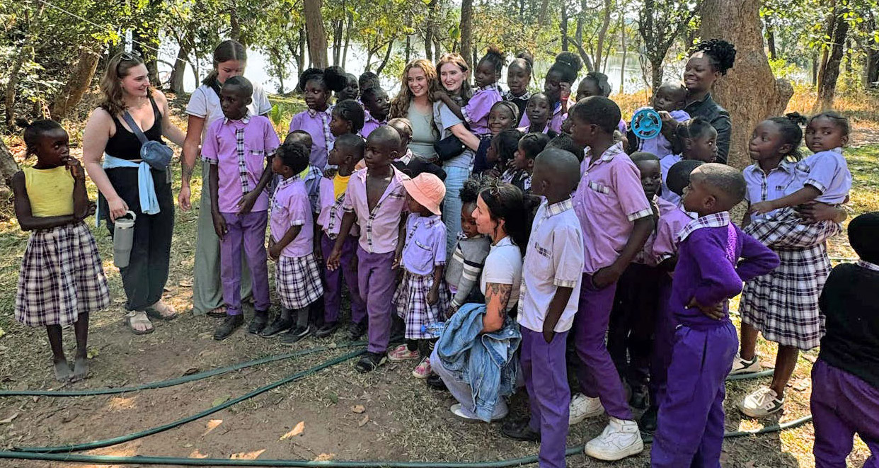 WSU College of Nursing students gather outdoors with Zambian children on a school field trip.