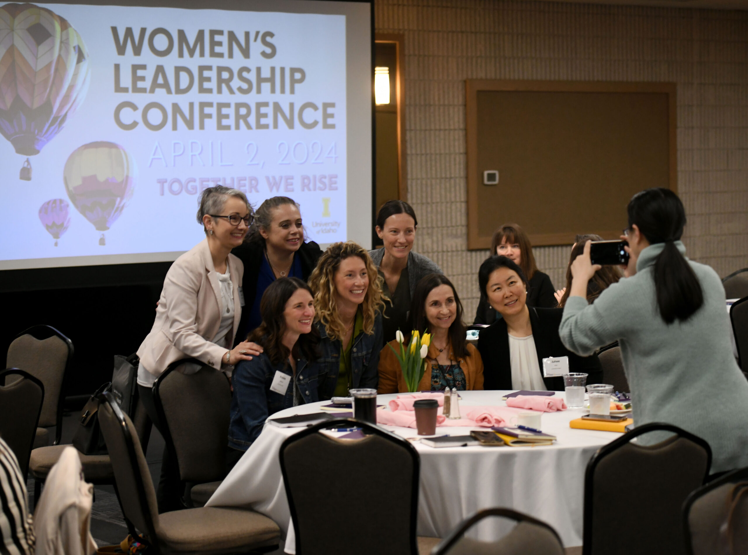 A group of women are taking a photo together around a large banquet table.