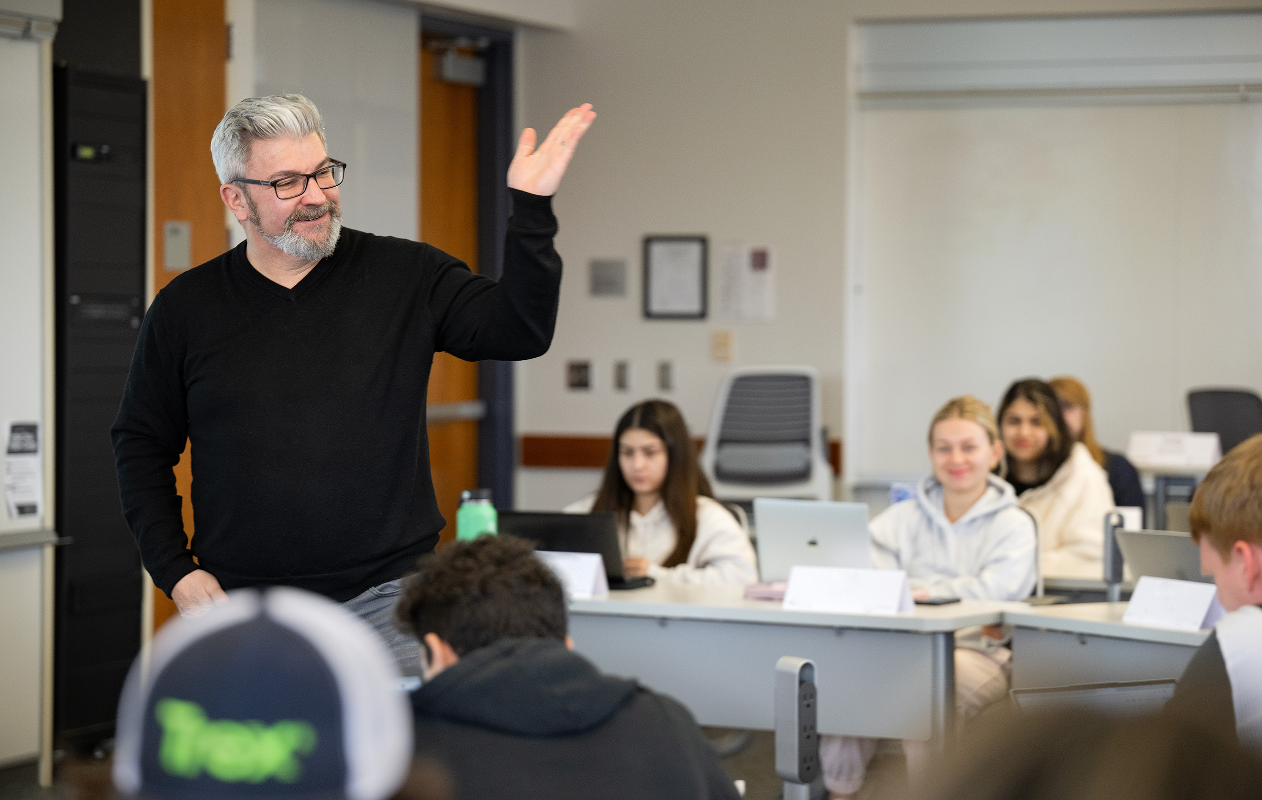 Carson College of Business Professor Chris Cooney lectures in class as students seated around him in desks look on and listen.