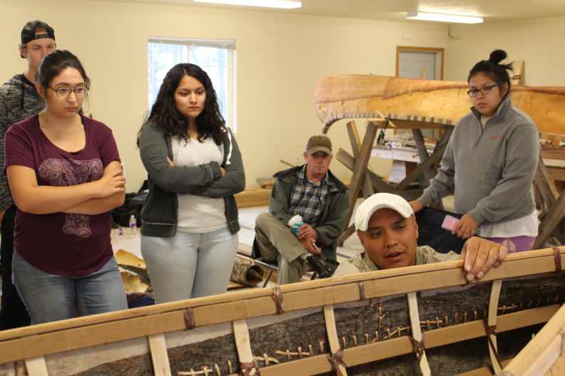 Dr. Brigman holds frame of canoe while students watch in background.