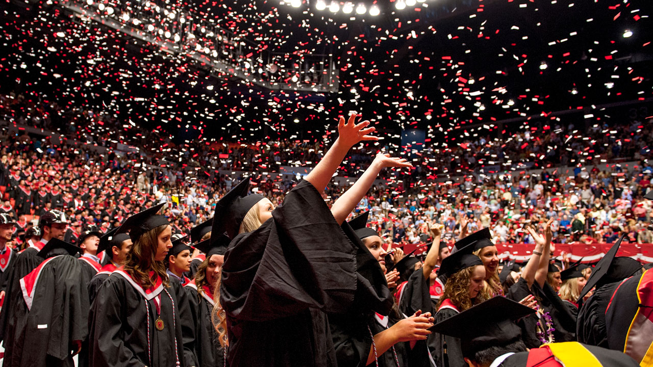 Newly graduated students throw up their hands in celebration at commencement.