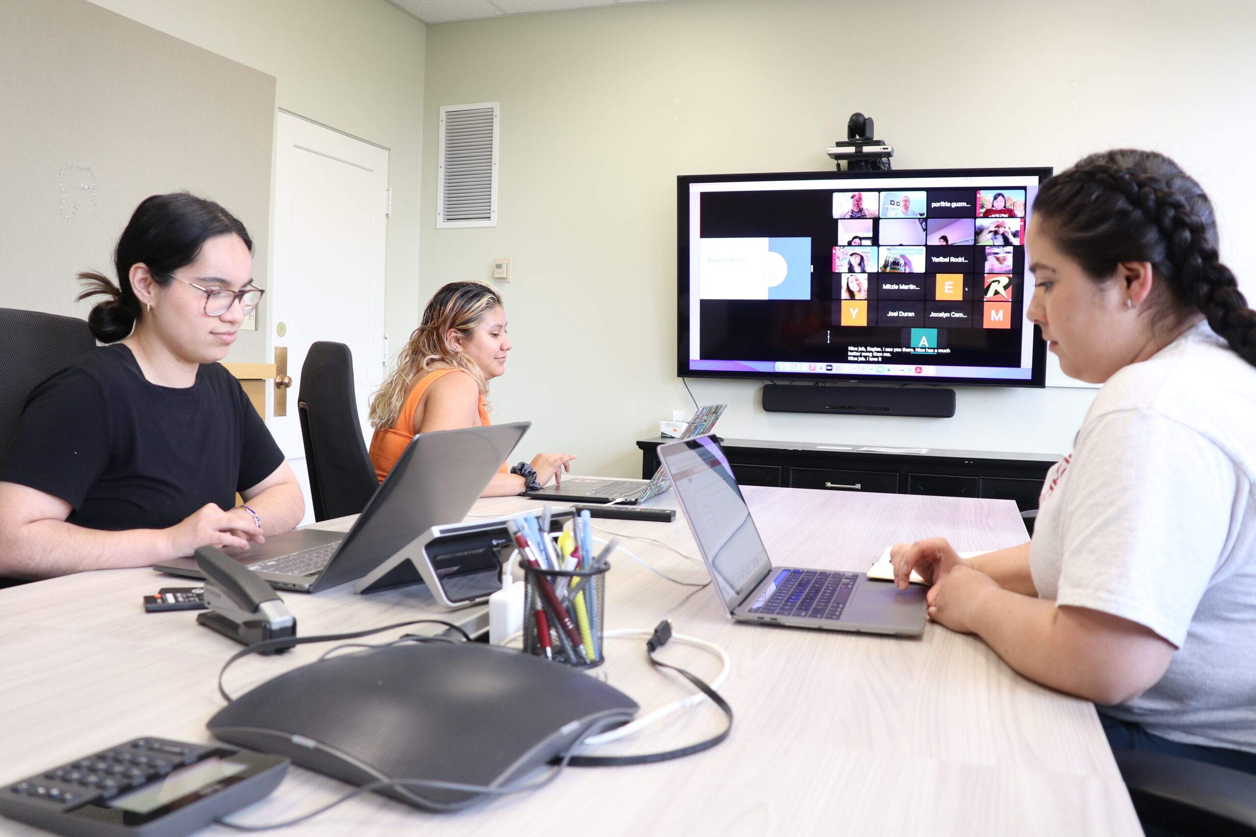 Students work on laptops in a classroom in front of a Zoom screen.