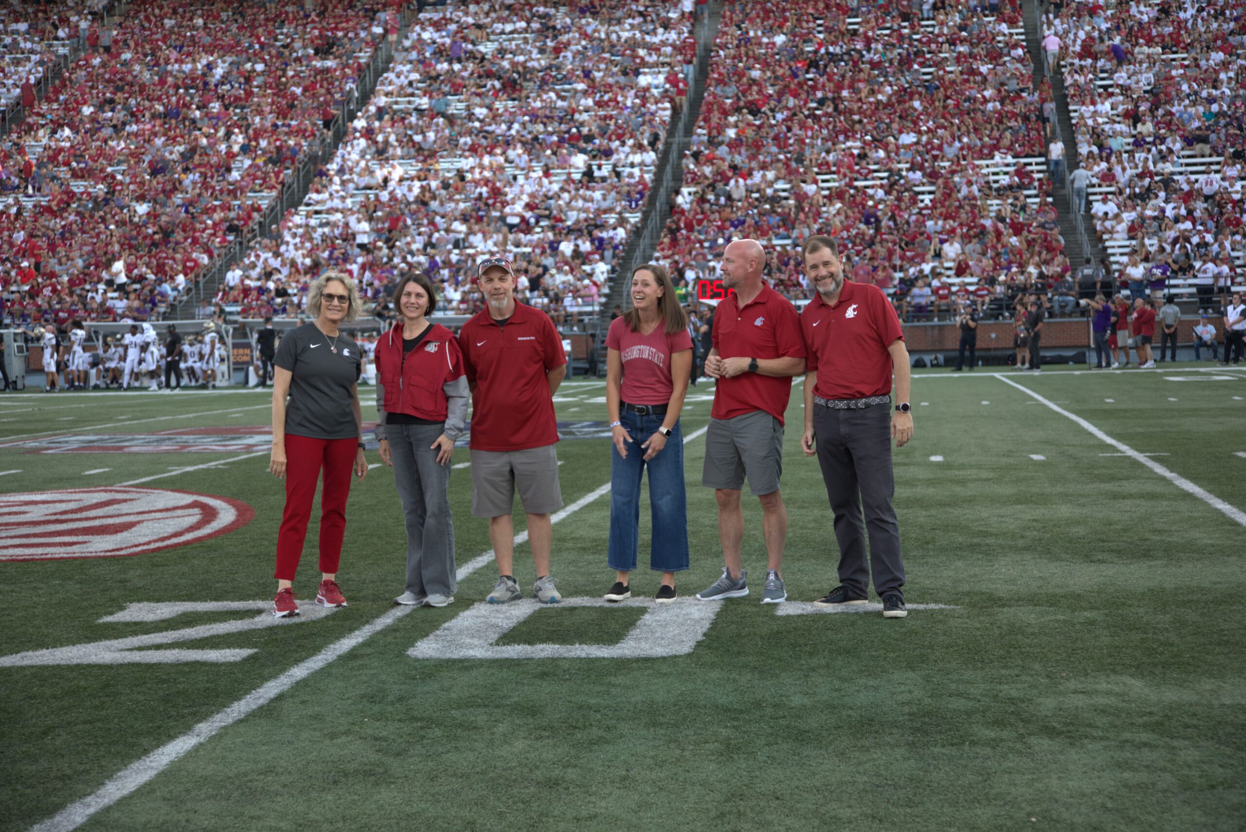 Provost Riley-Tillman, April Davis, Alana Pulay, their guests, and President Cantwell smile to the crowd at a Cougar football game on Gesa Field.