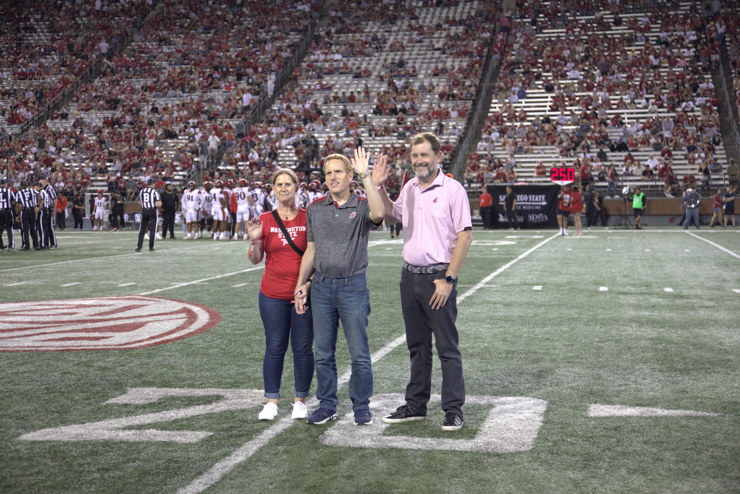 Provost Riley-Tillman, Kraig Jones, and his guest wave to the crowd at a Cougar football game on Gesa Field.