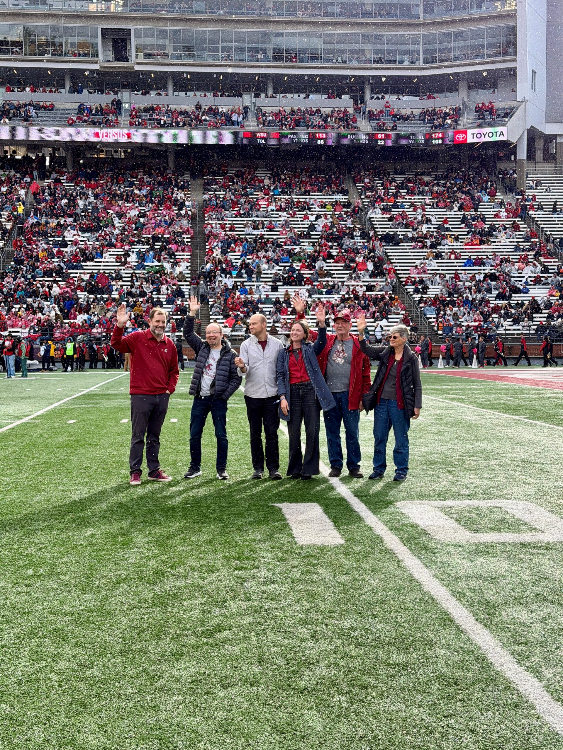 rovost Riley-Tillman, Will Gregg, Eugene Smelyansky, and their guests wave to the crowd at a Cougar football game on Gesa Field.