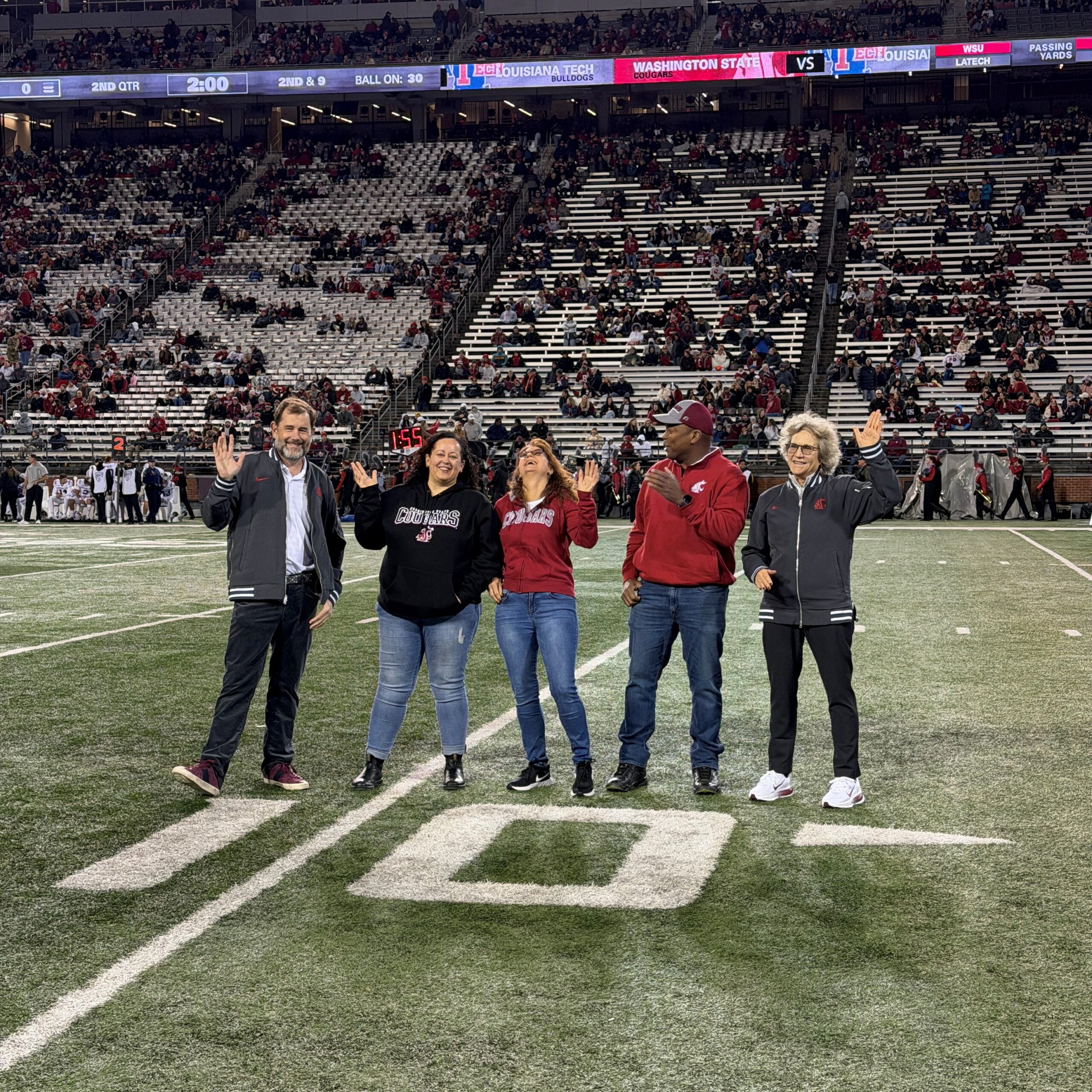 Provost Riley-Tillman, Melissa Jenkins, Christina Sanders, a guest, and President Cantwell wave to the crowd at a Cougar football game on Gesa Field.