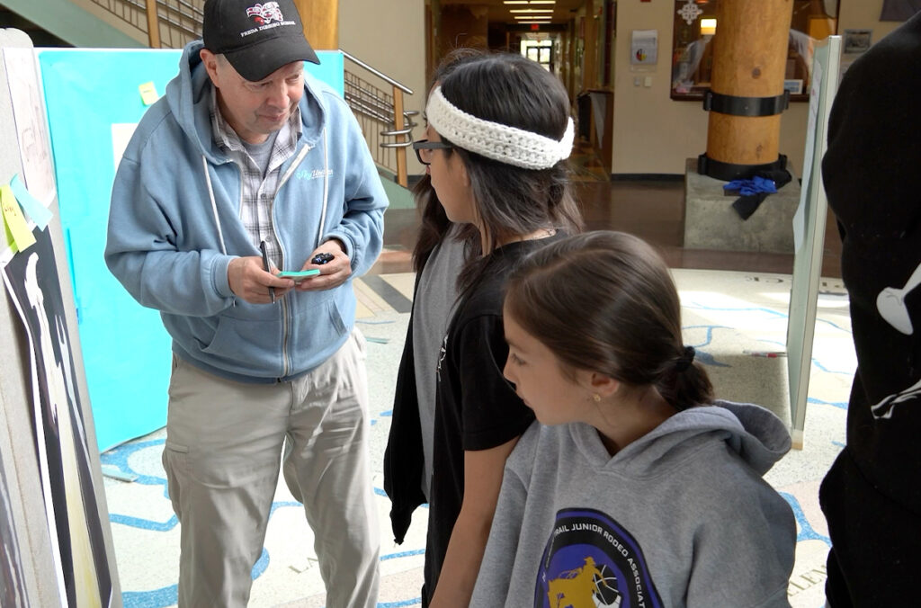 Art professor Michael Holloman speaks with three tribal youth curators in front of a work of art on exhibit.