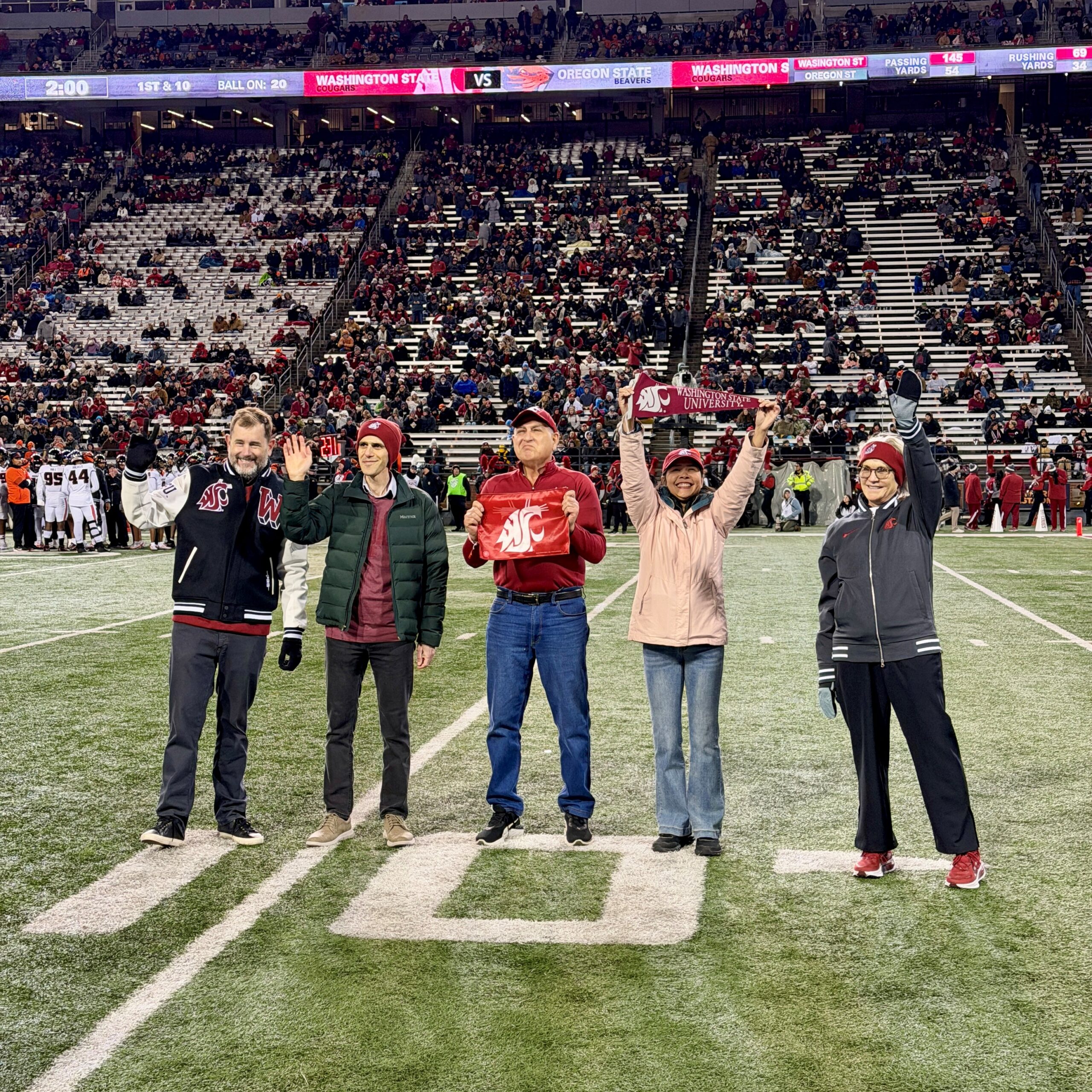 Provost Riley-Tillman, Mauricio Featherman, Aref Majdara, a guest, and President Cantwell wave to the crowd at a Cougar football game on Gesa Field.