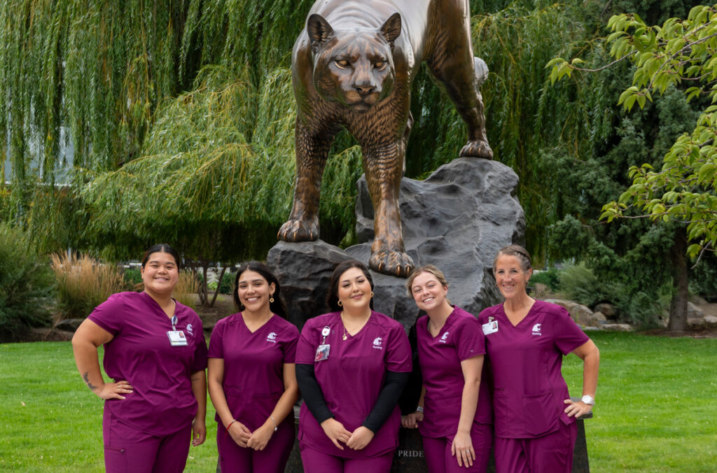 Five WSU nurses standing below a large statue of a cougar.