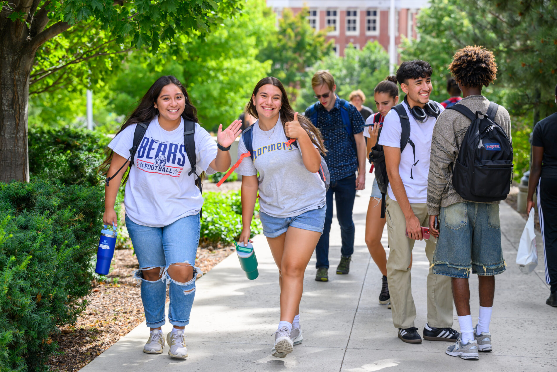 Two students smile and wave at the camera while two other students engage in conversation during  class change on the Pullman campus of Washington State University Pullman.