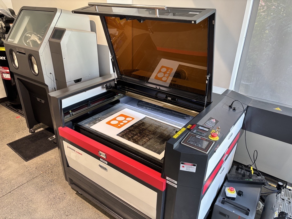 Large red, grey and white laser cutter and engraver with lid open showing a cutting surface.