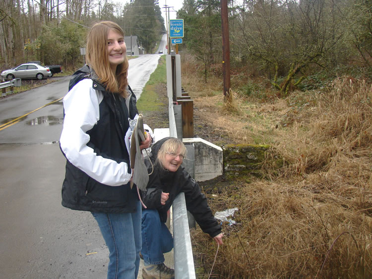 smiling people next to the metal divider by a road. one is standing and holds a clipboard and bait bag. link to full image