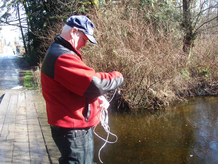a man preparing to tie a bait bag to the shore of a stream