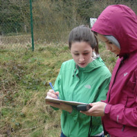 two girls in a field consult a clipboard